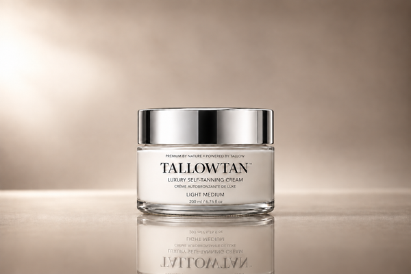 A glass jar of Tallowan Luxury Self-Tanning Cream with a reflective silver lid, set against a warm beige gradient background with a soft reflection below.