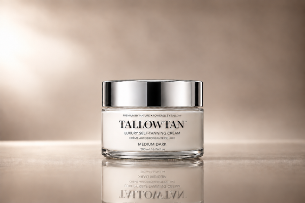 A glass jar of Tallowan Luxury Self-Tanning Cream with a shiny silver lid, set against a warm beige gradient background with a soft reflection below.
